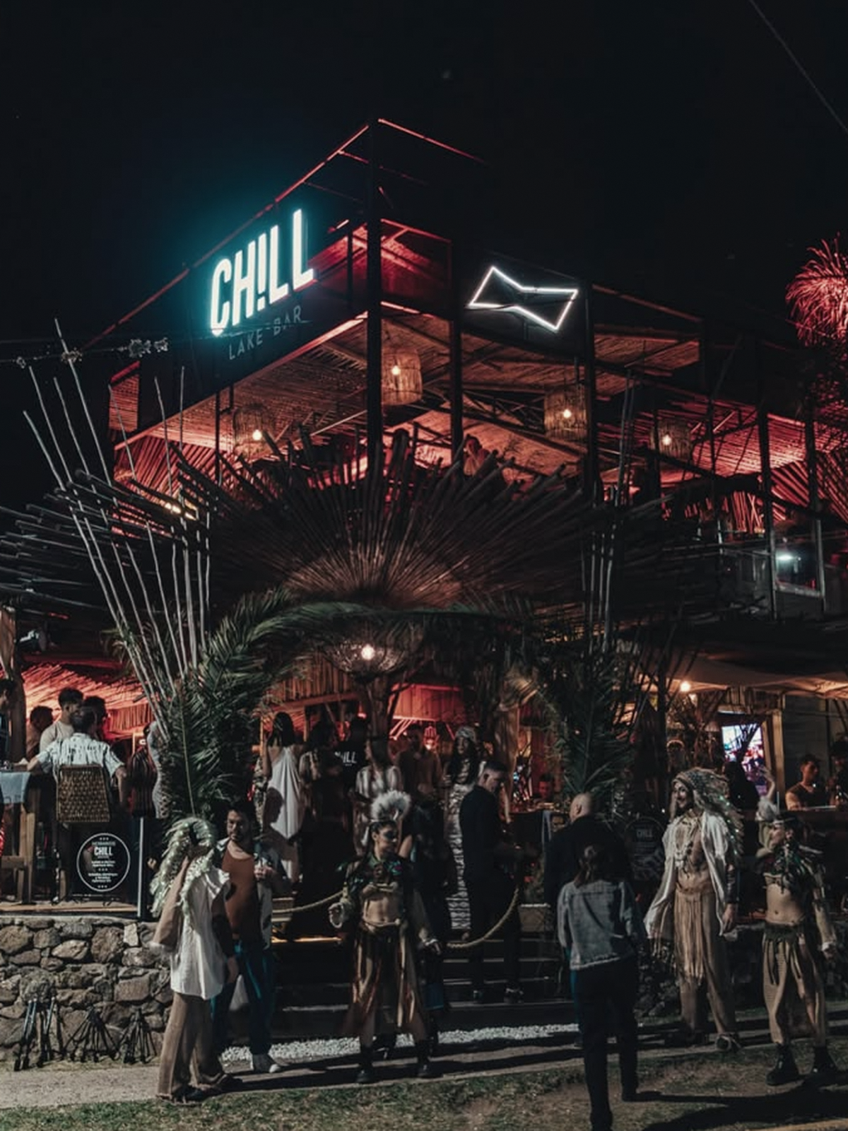 Fachada de dos pisos de Chill Lake Bar de noche, con letrero de neón y gente reunida en la entrada